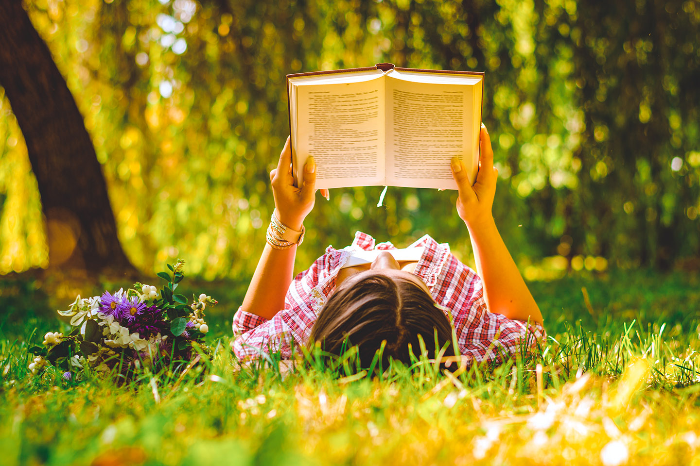 Young woman reading a book in the park with flowers